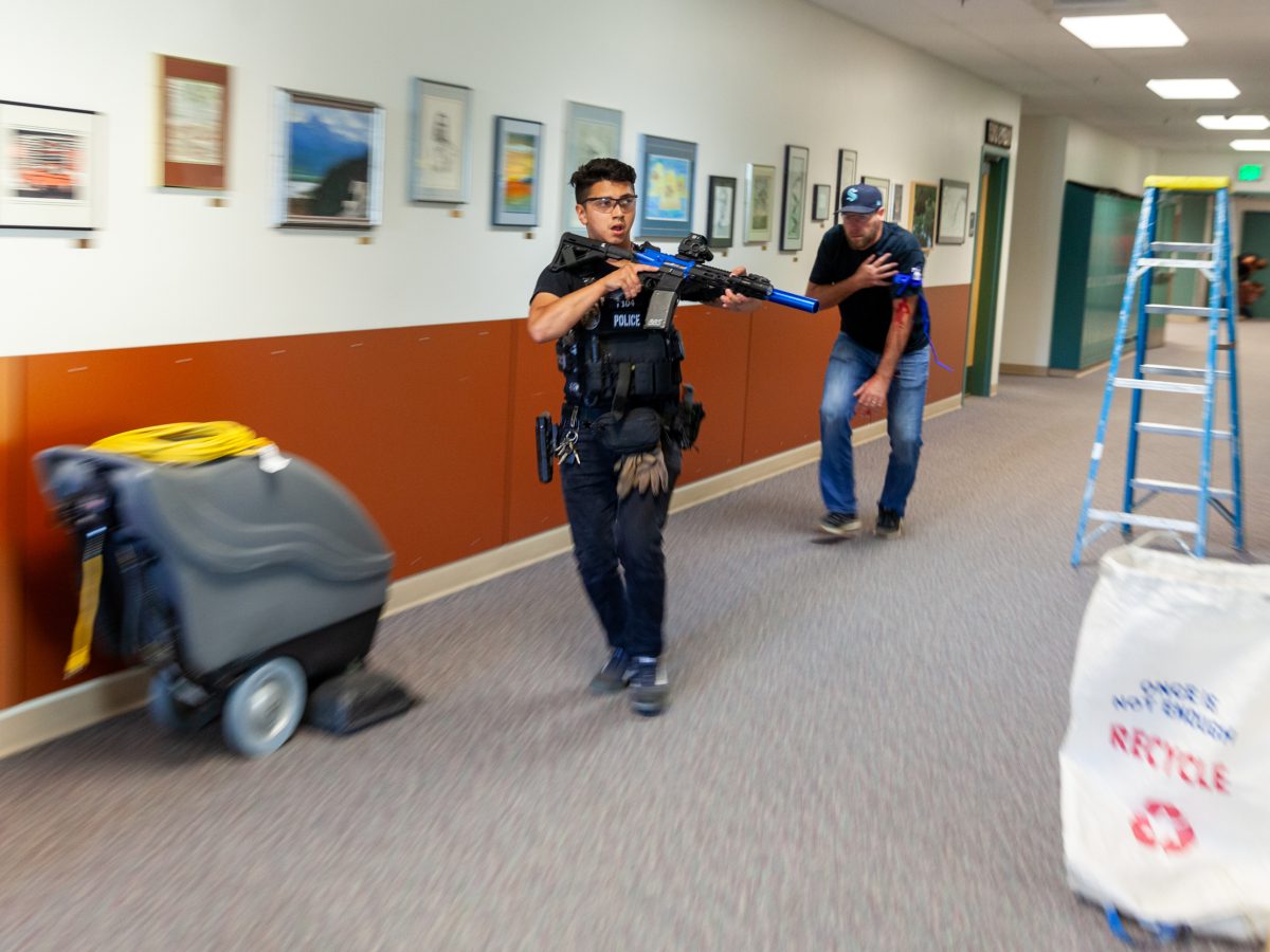 An officer with a simulation rifle moves through a school hallway as a volunteer shooting victim trails behind.